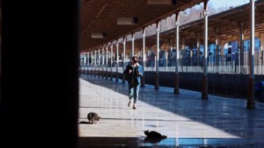 Genç bir gezgin açık hava tren istasyonunda yürüyor ve telefonuna bakıyor.