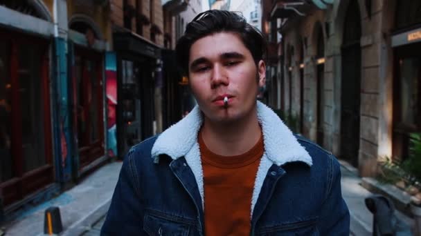 Un joven pretencioso fumando en la calle estrecha — Vídeos de Stock