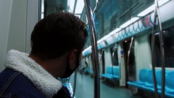 Un joven con máscara negra sentado en el tren del metro mirando a su alrededor — Vídeos de Stock