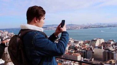 İstanbul 'un tepesinde genç bir adam duruyor ve telefonuyla manzaranın fotoğraflarını çekiyor.