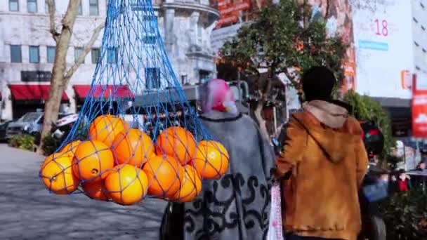 Πορτοκάλια στο δίκτυο στο προσκήνιο - οι άνθρωποι περπατούν στους δρόμους στο παρασκήνιο — Αρχείο Βίντεο