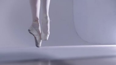 Genç bayan balerin, beyaz stüdyoda sivri uçlu ayakkabılarla yürüyor.