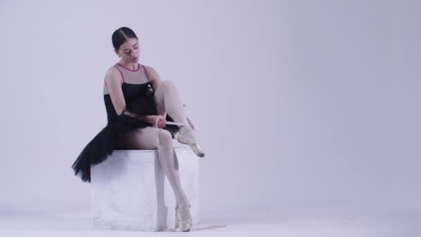 Bailarina joven en vestido negro poniéndose zapatos puntiagudos en el estudio blanco — Vídeo de stock