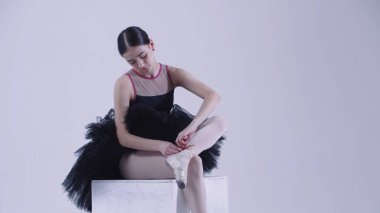 Siyah elbiseli genç bayan balerin stüdyoda sivri ayakkabılarını giyiyor.