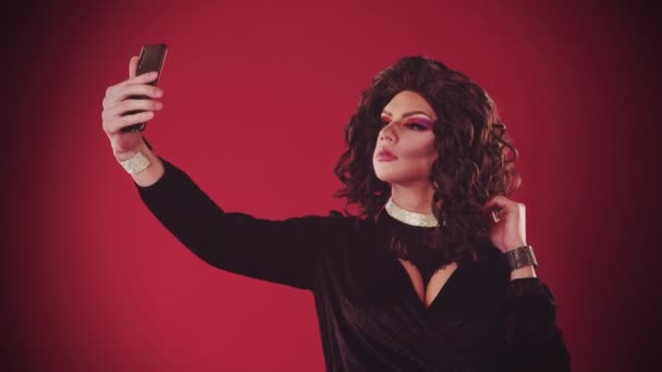 A young man drag artist in extravagant dress on the red background - taking a selfie and smiling — Stock Video