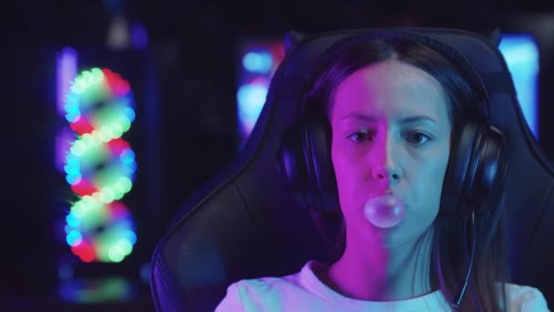 Young gamer woman sitting in a chair in gaming club and blowing a bubble gum — Stock Video