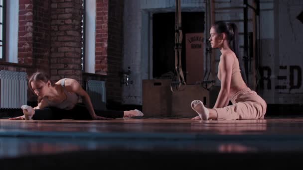 Dvě hubené ženy trénují společně v tělocvičně - protáhnou se před sebou - sedí v rozštěpení a natahují se po špičkách — Stock video