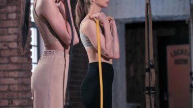 Spor salonunda birlikte antrenman yapan iki sıska kadın. Kemerde duran ve göğsüne doğru çeken el kaslarını çalıştırıyorlar.