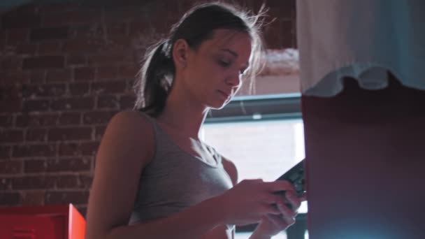 Une jeune femme met son téléphone dans un casier dans un vestiaire de gym, prend une serviette et s'en va — Video