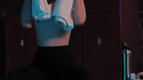 A young pretty woman sitting in locker room with a towel on her neck - looking in the camera — Stock Video