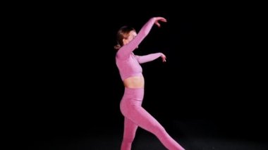 Jimnastik. Siyah stüdyoda dans eden genç plastik kadın.