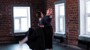 İki küçük balerin kız antrenmanda uzun siyah elbiseler içinde dans ediyor.