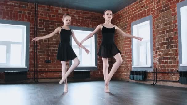 Ballet bailando en el interior - dos pequeñas chicas de gimnasia bailando sincrónicamente en traje negro en el entrenamiento — Vídeo de stock