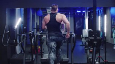 Sportif, kaslı bir adam spor salonundaki koşu bandında aynanın önünde koşar.