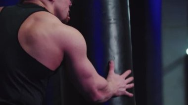 Koçla boks antrenmanı yapan bir kadın, koç onu tutarken kum torbasına vuruyor.