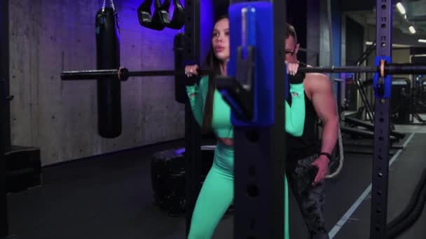 Gym training - woman trains her butt with dumbbell on her shoulders under the supervision of a trainer — Stok video