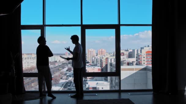 दो व्यापारी एक कार्यालय में पैरोनामी खिड़कियों के साथ खड़े हैं और सौदे पर चर्चा करते हैं — स्टॉक वीडियो