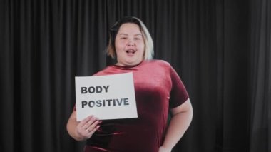 Kendine güveni tam, kilolu bir kadın elinde tabelalı bir tabela tutuyor.