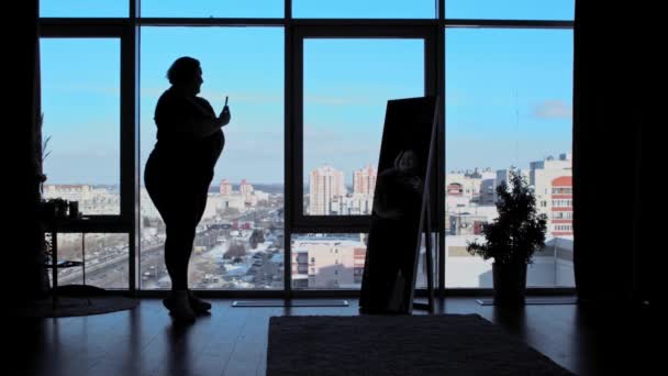 Una mujer con sobrepeso y confianza de pie en la oficina con ventanas panorámicas y tomando una foto en el espejo — Vídeo de stock