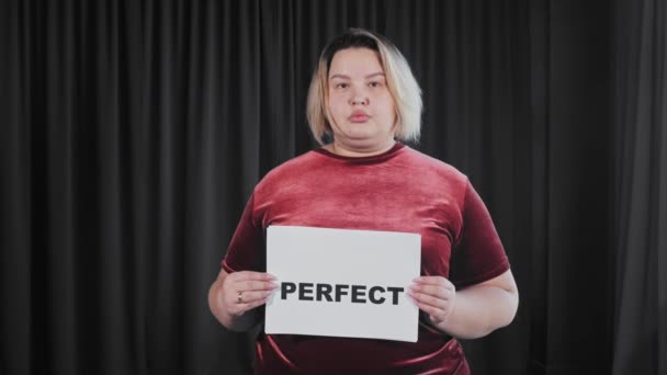 Uma mulher com excesso de peso confiante segurando uma placa com um sinal PERFEITO e REAL — Vídeo de Stock