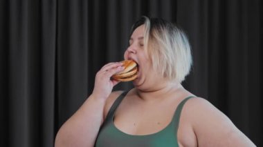 Gülümseyen şişman kadın elinde bir hamburger tutuyor ve yiyor. Vücut pozitifliği ve feminizmi.