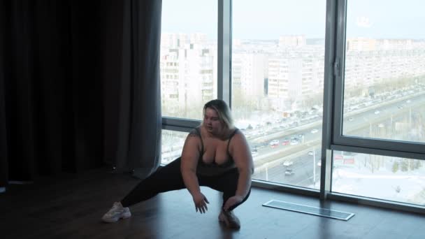 Μια υπέρβαρη γυναίκα με τατουάζ κάνει αθλητικές ασκήσεις στο στούντιο με πανοραμικά παράθυρα — Αρχείο Βίντεο