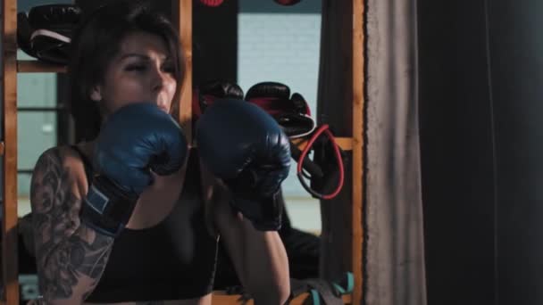 Boks - dövmeli bir kadın boksör eldiveni giyerek kum torbasına yumruk atıyor. — Stok video