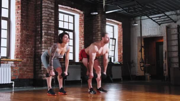 Couple dans la salle de gym - tenant des haltères et se penchant vers le bas - entraînement des mains — Video