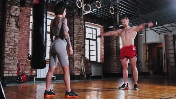 Athletic man and woman training in the gym together - doing hands exercises with dumbbells one at a time — Stock Video