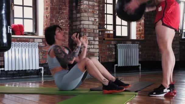 Un couple de formation dans la salle de gym femme tatouée pompage ses abdos et tenant la balle — Video