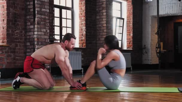 Ein Paar trainiert im Fitnessstudio - Frau pumpt ihren Bauch, während der Mann ihre Füße hält — Stockvideo