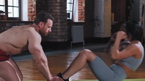 Een volwassen stel training in de sportschool - getatoeëerde vrouw pompen haar buikspieren, terwijl de man houdt haar voeten — Stockvideo