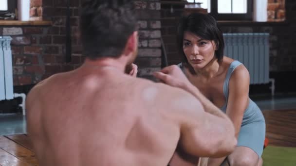 Un couple de formation dans la salle de gym homme pompage ses abdos tandis que la belle petite amie tenant ses pieds et regardant vers les côtés — Video