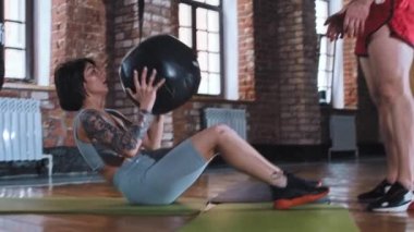 Spor salonunda antrenman yapan bir çift - karın kaslarını şişiren bir kadın - topu erkeğe atıyor ve topu geri atıyor.