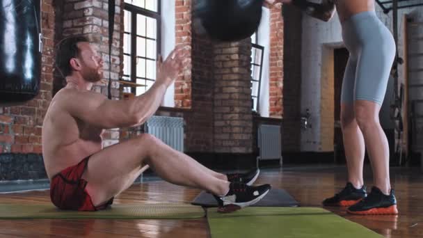 Ein Paar trainiert im Fitnessstudio - Mann pumpt seinen Bauch - wirft der Frau den Ball zu und wirft ihn zurück — Stockvideo