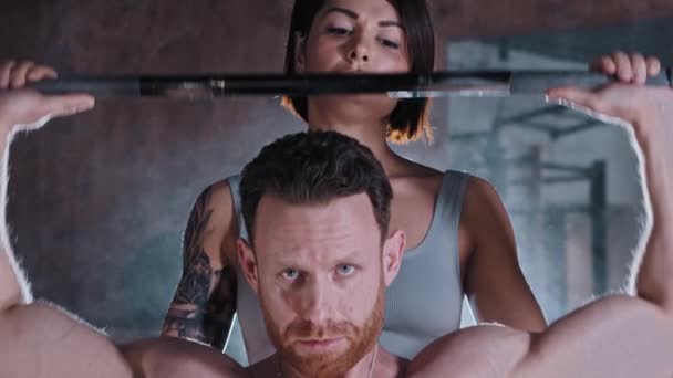 Çekici bir yetişkin çift spor salonunda antrenman yapıyor. Atletik bir adam ellerini bir dambıl ile şişiriyor ve dövmeli bir kadın arkasında duruyor. — Stok video