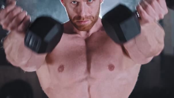 An athletic adult attractive man pumping his hands muscles with dumbbells — Stock Video