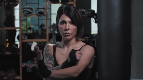 Tetovaná žena stojí v bojové póze a ukazuje svůj pohyb v boxerské tělocvičně — Stock video