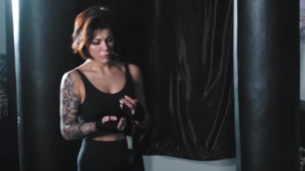 Татуированная женщина связывает руки и стоит в боевой позе - глядя в камеру — стоковое видео