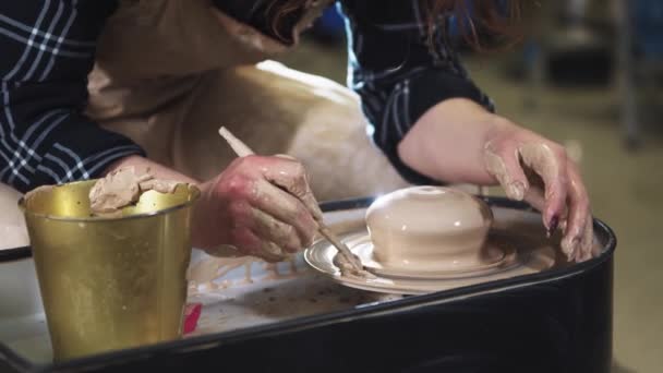 Een vrouw verwijdert de klei overtollige van een pottenbakkerswiel met een stok — Stockvideo