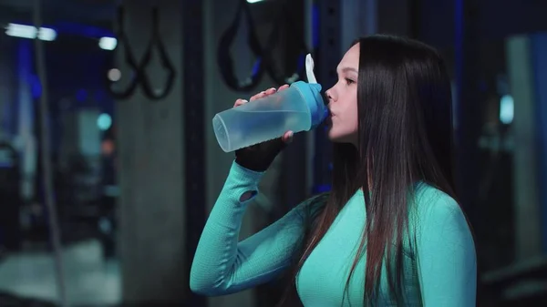 Uma mulher em trajes esportivos bebendo água no ginásio — Fotografia de Stock
