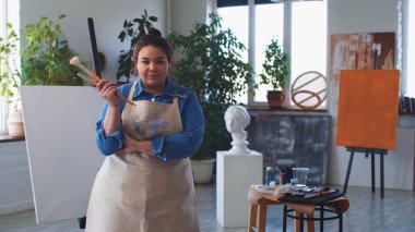 Elinde fırçalarla poz veren ve kameraya bakan bir kadın ressam.