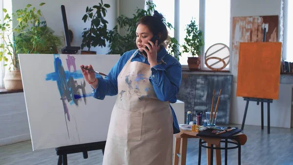Una mujer pintora hablando en su teléfono mientras dibuja una pintura —  Fotos de Stock