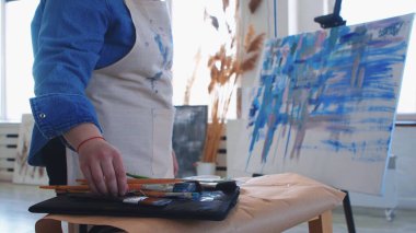 Bir kadın ressam masadan fırça alıyor.