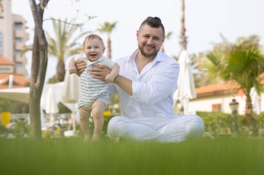 Mutlu baba ve tatlı oğlu çimlerin üzerinde oturup kameraya bakıyorlar.