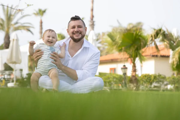 Щасливий батько і його син сидять на траві дивлячись в камеру — стокове фото