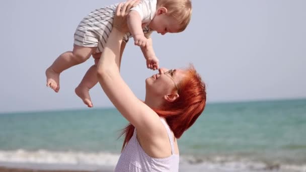 Šťastná matka vychovávat svého malého syna sedí na pláži — Stock video