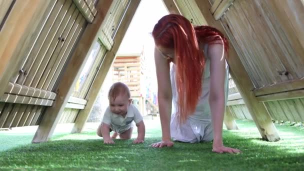 Copil drăguț și mama lui târându-se sub un acoperiș de lemn pe terenul de joacă — Videoclip de stoc
