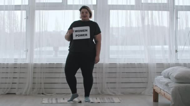Concepto de positividad corporal - una mujer gordita sonriente sostiene un signo con la inscripción MUJERES PODER — Vídeo de stock