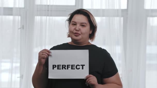 Positif tubuh konsep - seorang wanita tersenyum gemuk memegang tanda dengan tulisan PERFECT - melihat ke kamera — Stok Video